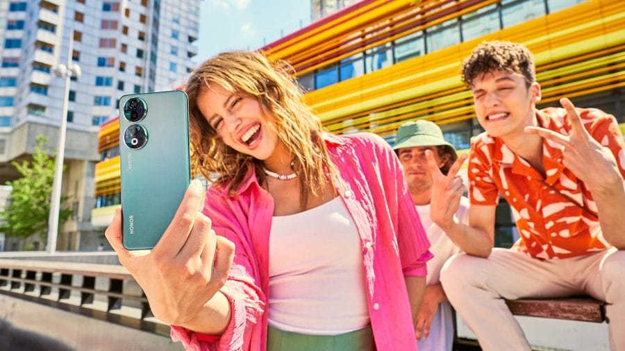 Foto de estilo de vida de teléfono inteligente de HONOR 90 de una mujer que usa un teléfono inteligente y un grupo en segundo plano