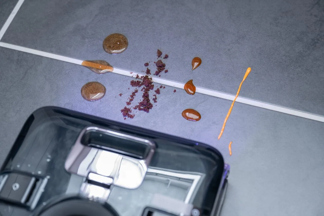 Roborock F25 Ultra framför ett testområde med cola, kaffesump, ketchup och majonnäs